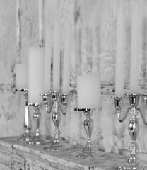 Fototapeta na wymiar White candles in elegant candlesticks stand on a fireplace