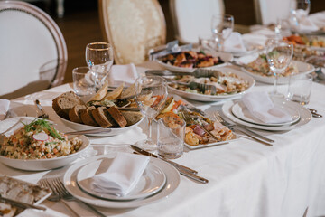 Table setting for a banquet or celebration.Empty glasses for alcoholic beverages, wine and juice, a set table.Cloth napkins on a white platter and cutlery on the table.Cold appetizers and salads