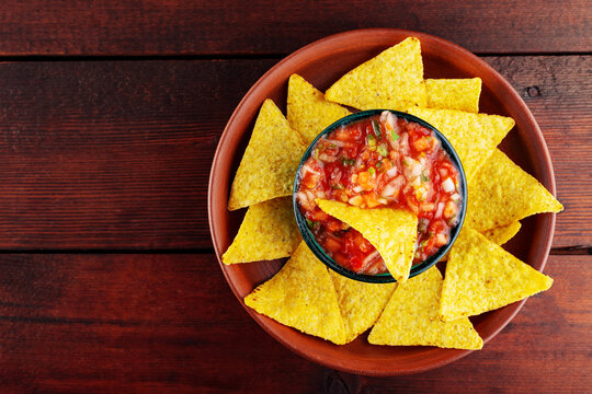 Salsa sauce and nacho chips in a clay bowl. Tortilla chips and salsa dip in bowl on brown boards. Top view. Copy space