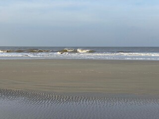 Hinter einem Priel brechen Wellen im Herbst am Strand der Nordseeinsel Borkum. 