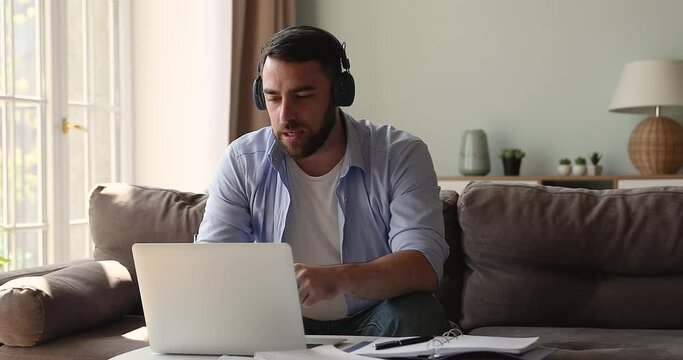 Young man service line manager working from home remotely wear headphones answer customer question give technical support using laptop. Male expert meet client online help to solve problem on distance