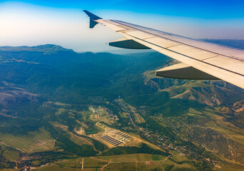 Fototapeta premium View of airplane wing, blue skies and green land during landing. Airplane window view.