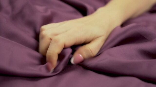 Female Hand In A Burst Of Passion Squeezes Silk Linens On Bed, Woman Makes Love And Orgasms. Close-up of Hand. Woman Climaxes.