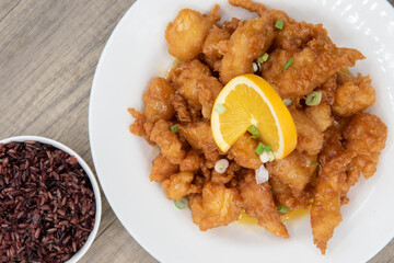 Overhead view of breaded orange chicken crispy on the outside with sliced citrus twist on top of generous pile of food