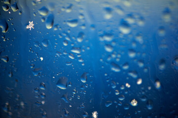 Abstract background with rain drops and snowflakes on car window, wet glass, rainy day.
