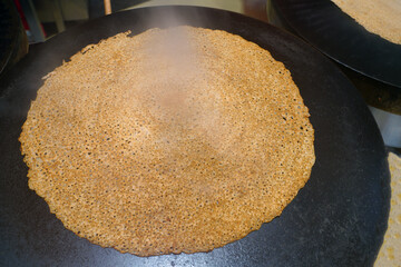 A buckwheat galette cooking on a traditional crepe griddle in Brittany, France