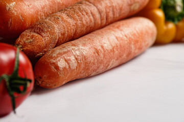 Close up of carrots, between red tomato and yellow bell pepper. Isolated on white background.