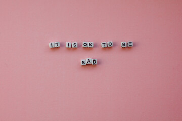 Motivational sentence "it is ok to be sad" - white letters on a pink background