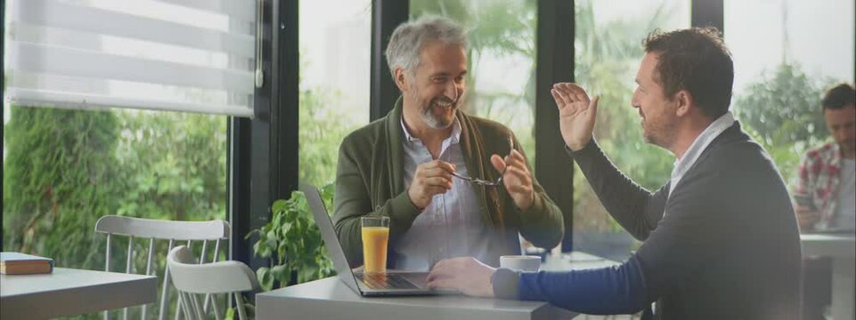 Two smiling satisfied gentlemen discussing business over laptop in cafe. Make a deal. Entrepreneur working outside office.