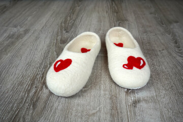 Fototapeta na wymiar Felt white slippers with red hearts on the floor. Valentine's day gift