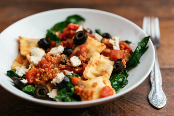 Bowl with vegan ravioli with spinach, TVP, olives, a tomato sauce and home made vegan feta.