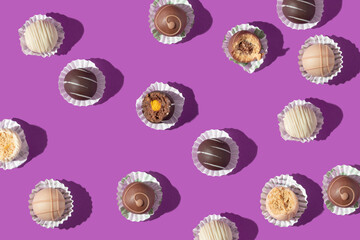Valentines day creative pattern with chocolate pralines on bold purple background. 80s or 90s retro fashion aesthetic love and sweets concept. Minimal romantic idea chocolate.