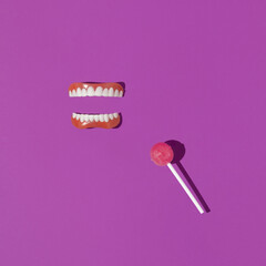 Creative layout with false teeth and lollipop on bright purple background. 80s or 90s retro aesthetic concept. Surreal idea with lollipop