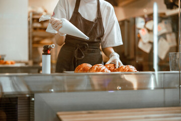 Lady holds sleeve with white cream ready to decorate croissants in bakery shop