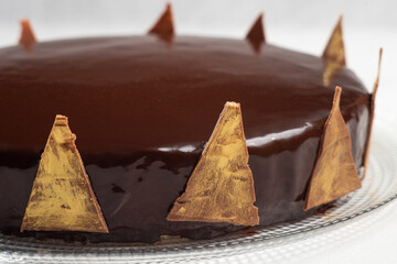 Homemade mousse cake with mirror chocolate coating decorated with chocolate triangles painted with edible gold, concept of lactose-free homemade dessert