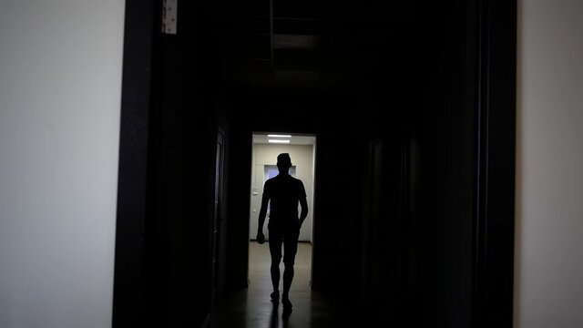 Backlit young man walks down the long corridor to the exit and out the door.