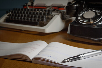 Checkbook, ink pen, retro typewriter and old telephone on the table.  Selected focus