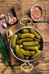 Pickled gherkins cucumbers in bowl with herbs. Wooden background. Top view
