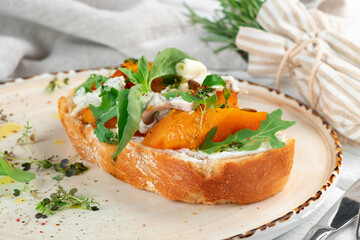 Bruschetta with fried pumpkin, cottage cheese and arugula on rye bread on a plate. Vegetarian Sandwich for breakfast with pumpkin, close up