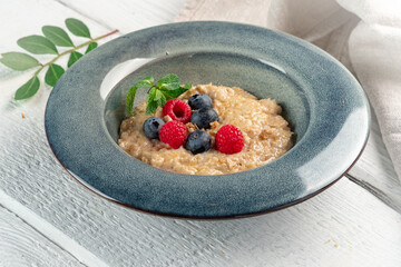 Oatmeal porridge with fresh blueberries, raspberries, mint.and nuts in a blue bowl on a wooden table. Vegetarian breakfast and healthy food with fiber