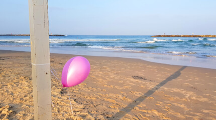 Pink color single balloon tied to a pole on the sea beach