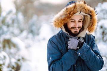 Handsome bearded young  man standing outdoors fur hood in winter season forest. Season holiday...