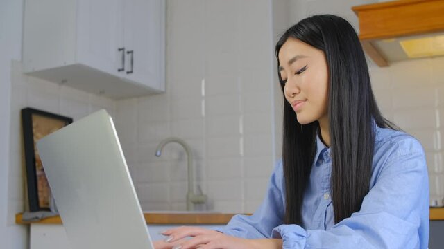Beautiful young asian woman working on laptop. Distant learning concept filmed in 4k. Cute Vietnamese girl typing on notebook pc at home. Freelancer female work at home. BIPOC person lifestyle video