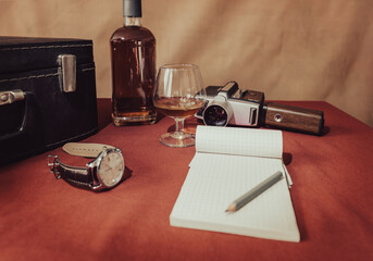 Bottle, glass, wrist watch, notebook and old movie camera on red table. Still Life. Retro composition