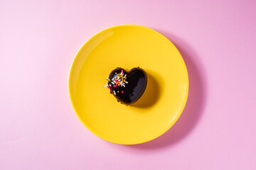 Heart shaped chocolate cake on a yellow plate with heart shaped chocolate pralines on a purple background with two red ribbons. Great concept for Valentine day or anniversary of love or wedding