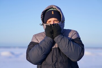 Portrait of frozen guy, handsome freezing man standing walking outdoors at north at winter snowy cold frosty day, shaking, trembling, shivering because of extreme low temperature in jacket, hat, hood