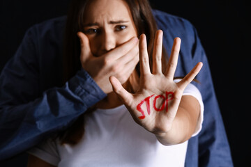 Man covering mouth of scared young woman on dark background. Violence concept
