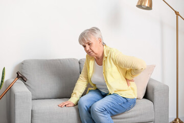 Senior woman suffering from back pain on sofa at home