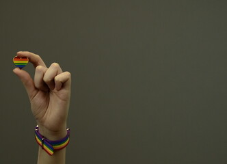 LGBT rainbow heart symbol of love in hands. Female hand with a rainbow bracelet. Love symbol. Gray background.