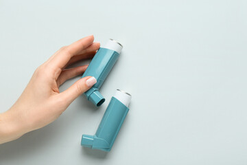 Female hand with modern asthma inhalers on grey background