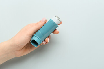 Female hand with modern asthma inhaler on grey background