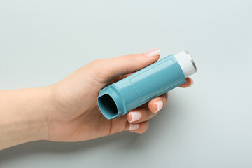 Female hand with modern asthma inhaler on grey background