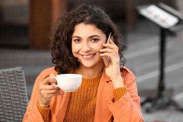 Beautiful woman drinking tea and talking by phone in street cafe