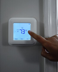 Person adjusting the home temperature on a smart thermostat - 479240330