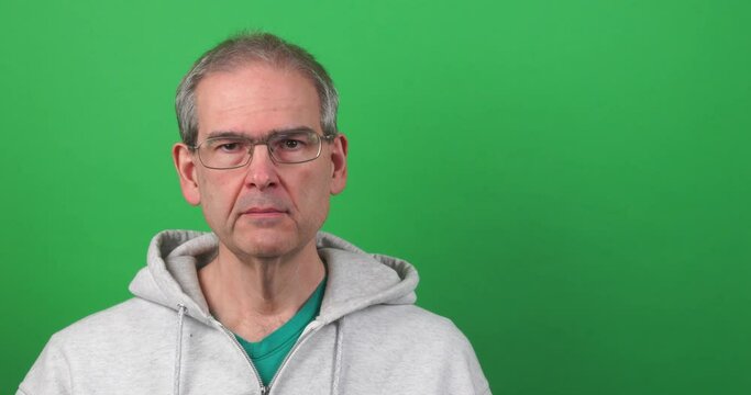 Funny clip of a man on a green screen making a face and holding up a heart decoration. High-quality 4k footage of a casual man in his late 50's mocking valentines day.