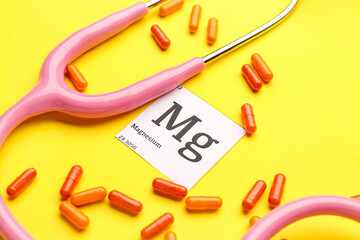 Magnesium pills and stethoscope on yellow background, closeup