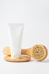 Dry massage brush made of natural materials and cream in cosmetic tube on a white background. Spa concept, body skin care. Minimalism, copy space.