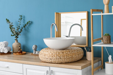 Rattan stand with sink, mirror and bath supplies near blue wall