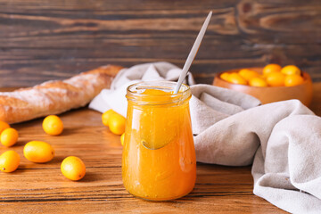 Jar of tasty kumquat jam and fresh fruits on wooden background