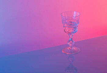 Glass against neon iridescent pink and blue colors. Minimal  party life concept.