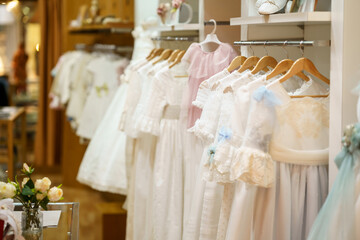 Fototapeta na wymiar Display rack with first communion dresses for girls in a luxury children's clothing shop.