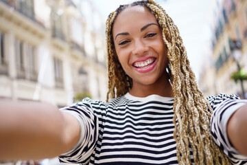 Black girl with afro braids taking a selfie in an urban street with a smartphone.
