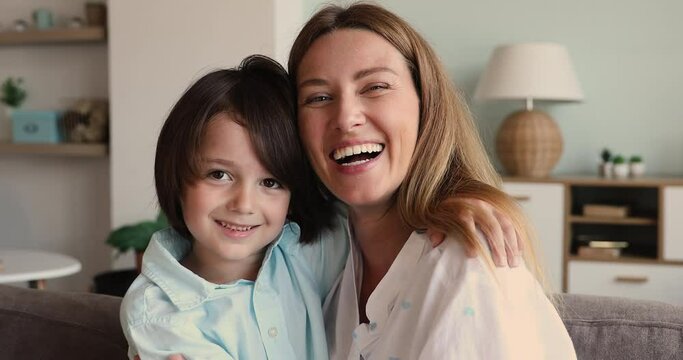 Portrait of affectionate young mother sit on sofa at cozy home embrace hold in arms cute little kid preschool age son look at camera with smile. Kind foster mom nanny hug little boy enjoy motherhood
