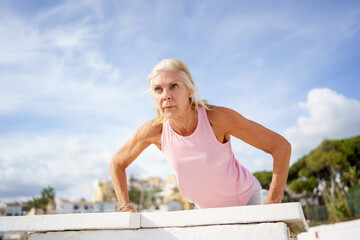 Mature woman working strength training push ups against sky with copyspace.