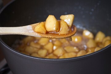 Bamboo spoon with cooked apple pieces above casserole pot with apple compote - obrazy, fototapety, plakaty