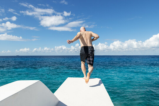 Shirtless man runs on diving platform to jump into vibrant blue Caribbean ocean water on the tropical island of Cozumel, Mexico